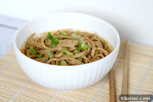 thai peanut noodles - A vibrant dish of whole wheat noodles coated in a rich, homemade Thai peanut sauce, garnished with fresh green onions and sesame seeds.