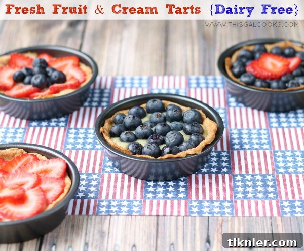 Beautifully presented Dairy-Free Fruit and Cream Tarts on a serving platter surrounded by fresh mint and berries