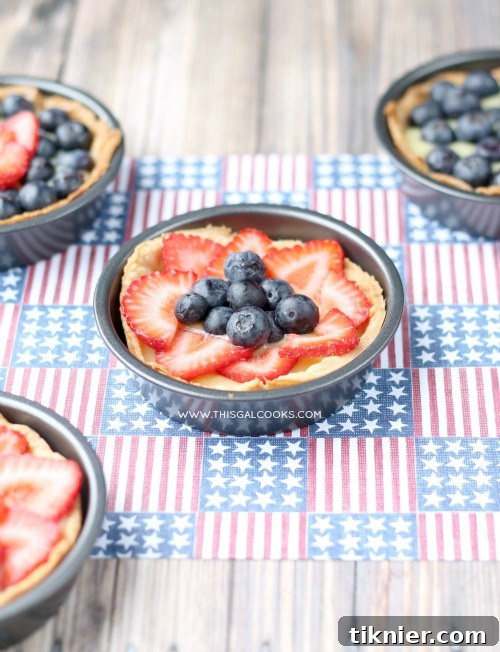 Overhead view of multiple Dairy-Free Fresh Fruit Tarts on a rustic wooden board with scattered fresh berries and mint leaves