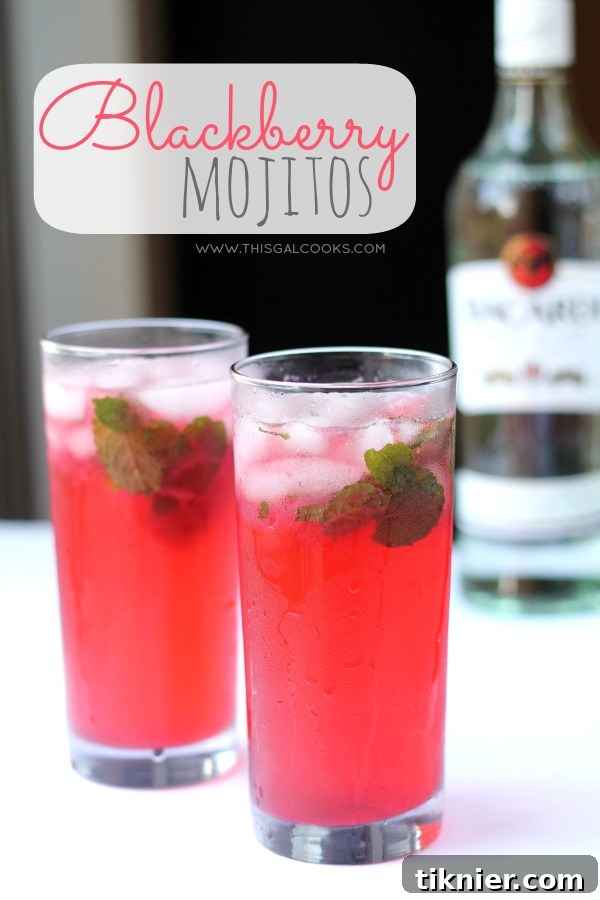 A beautifully presented Blackberry Mojito in a tall glass, garnished with fresh mint leaves, lime wedges, and whole blackberries. The drink is a vibrant purple, suggesting its fresh fruit content, and condensation beads on the glass highlight its chilled nature.