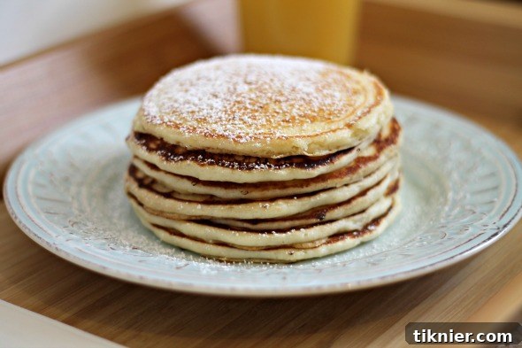 Fluffy white chocolate pancakes topped with powdered sugar and berries, a sweet and delightful breakfast from This Gal Cooks.