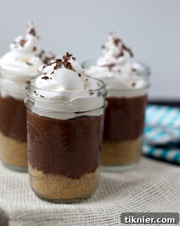 Three Chocolate Pudding Pie In A Jar desserts arranged on a wooden board, garnished with whipped cream and chocolate shavings.