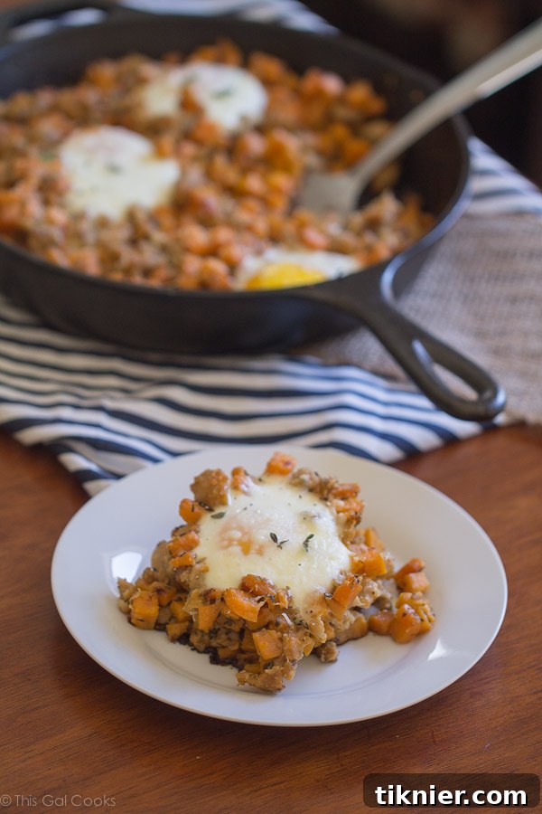 A vibrant close-up of the finished Chicken Sausage and Sweet Potato Hash with a perfectly runny baked egg and fresh thyme garnish, ready to be served.