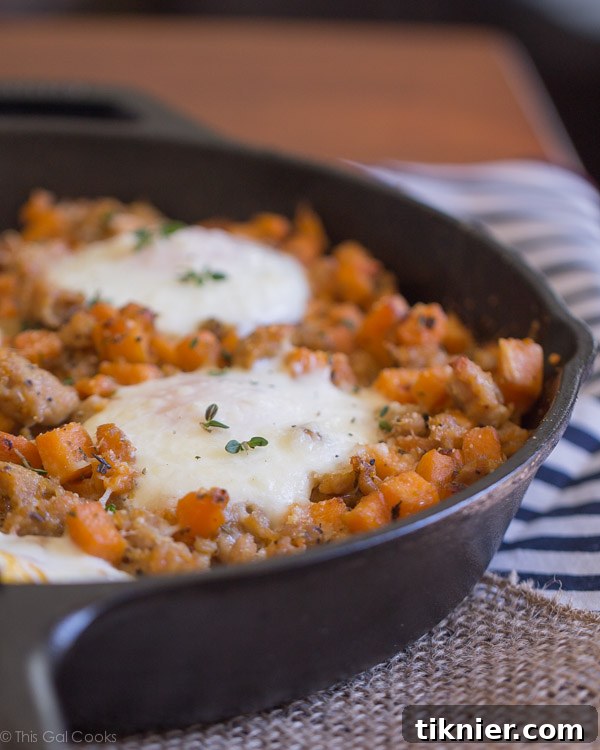 A generous serving of Chicken Sausage and Sweet Potato Hash with Baked Eggs, presented in a bowl with a fork, emphasizing its inviting texture and appetizing appearance.