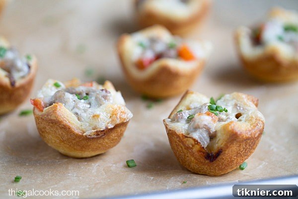 A top-down view of several baked Cheesesteak Crescent Roll Cups, garnished with fresh chives, in a mini muffin pan.