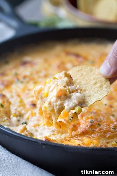 A bowl of the BEST Cheesy Chipotle Shrimp & Corn Dip, perfect for game day, surrounded by tortilla chips.