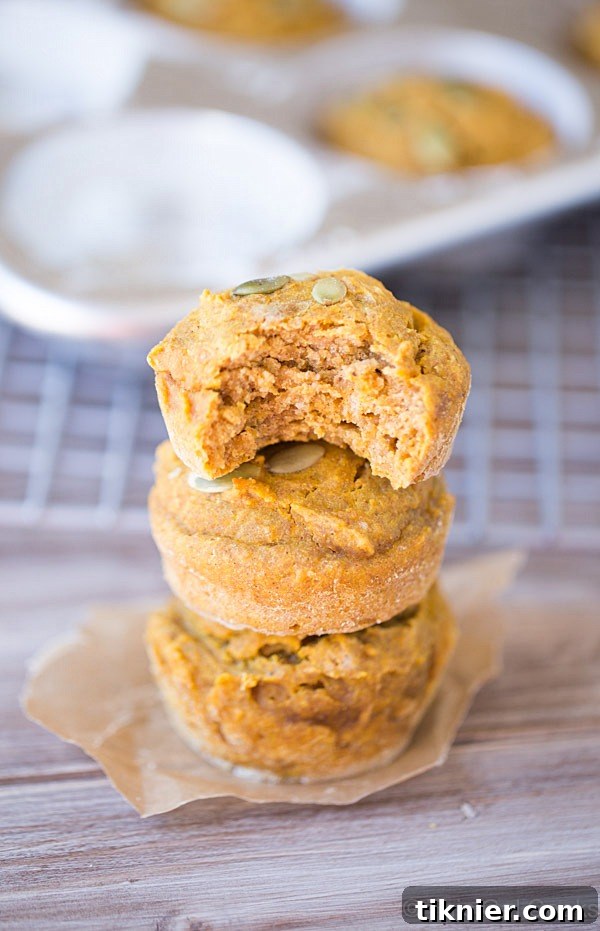 Stack of healthier pumpkin muffins, showing the fluffy interior and golden crust, topped with crunchy pepitas.