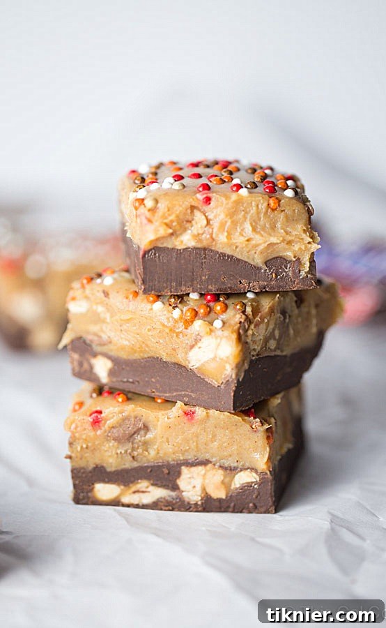 Close-up of Snickers Chocolate Peanut Butter Pumpkin Fudge, showing the distinct chocolate and pumpkin layers, studded with Snickers pieces. An easy-to-make dessert for any occasion.