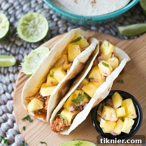 Main image for the Slow Cooker Shredded Chicken Tacos recipe featuring succulent chicken and bright pineapple salsa on tortillas.