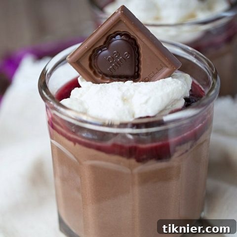 Velvety homemade chocolate pudding with a swirl of cherry sauce and fluffy whipped cream, adorned with a Ghirardelli chocolate square.