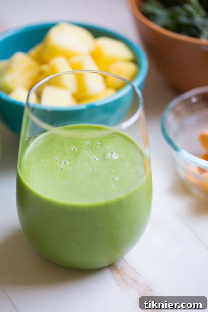 Two glasses of Tropical Kale Smoothie, garnished with a slice of pineapple and fresh kale, highlighting its beautiful green color and creamy texture.