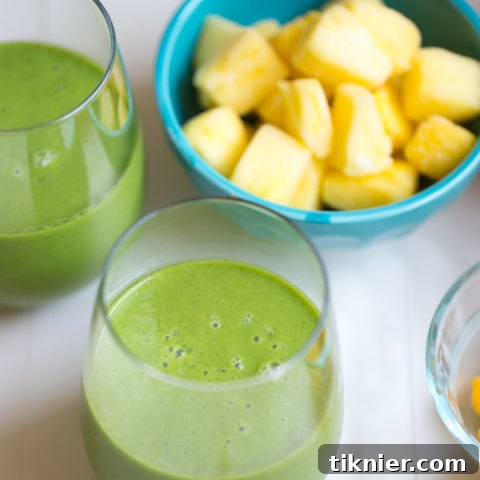 A vibrant green Tropical Kale Smoothie in a clear glass with a straw, garnished with fresh kale and tropical fruit slices.