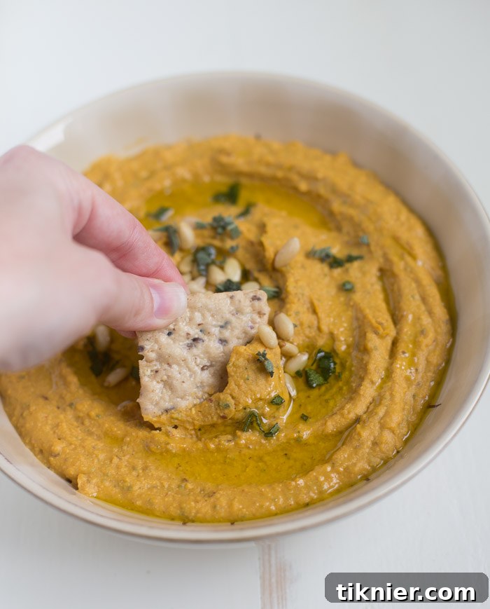 Homemade Pumpkin Hummus garnished with fresh sage and tart cranberries, perfect for a fall gathering.