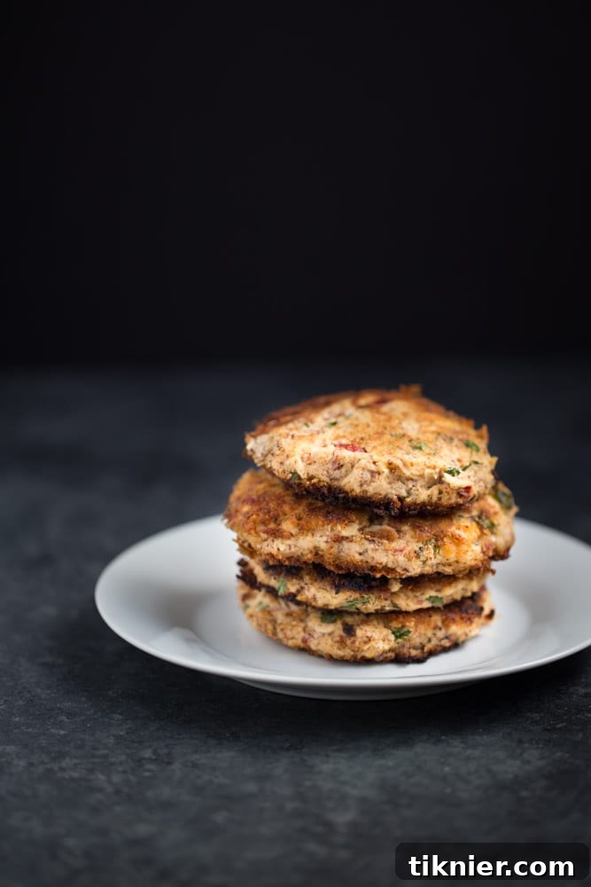 FLAVORFUL Easy Tuna Cakes are paleo + gluten free. Great for lunch or to serve as an appetizer! A close-up of a plate with two golden-brown tuna cakes and a side of dipping sauce.