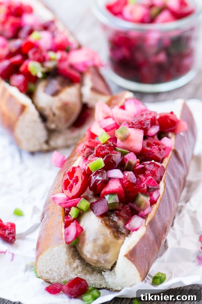 Grilled Brats generously topped with a vibrant, chunky Spicy Cranberry Relish, served on toasted buns with a side of greens.