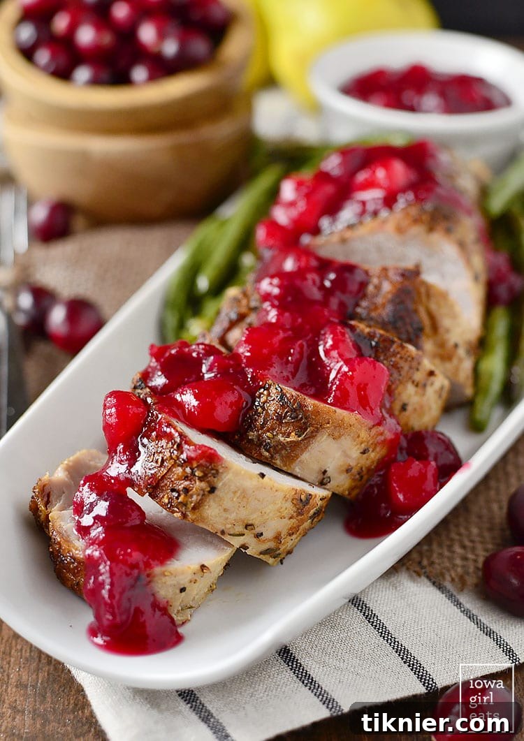 Perfectly sliced Roasted Pork Tenderloin, glistening with a vibrant Cranberry-Pear Sauce, garnished with fresh rosemary.