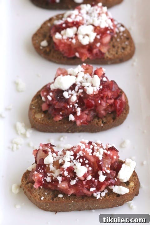 Appetizing Cranberry Goat Cheese Crostini garnished with fresh thyme and a light drizzle, presented neatly on a serving board.