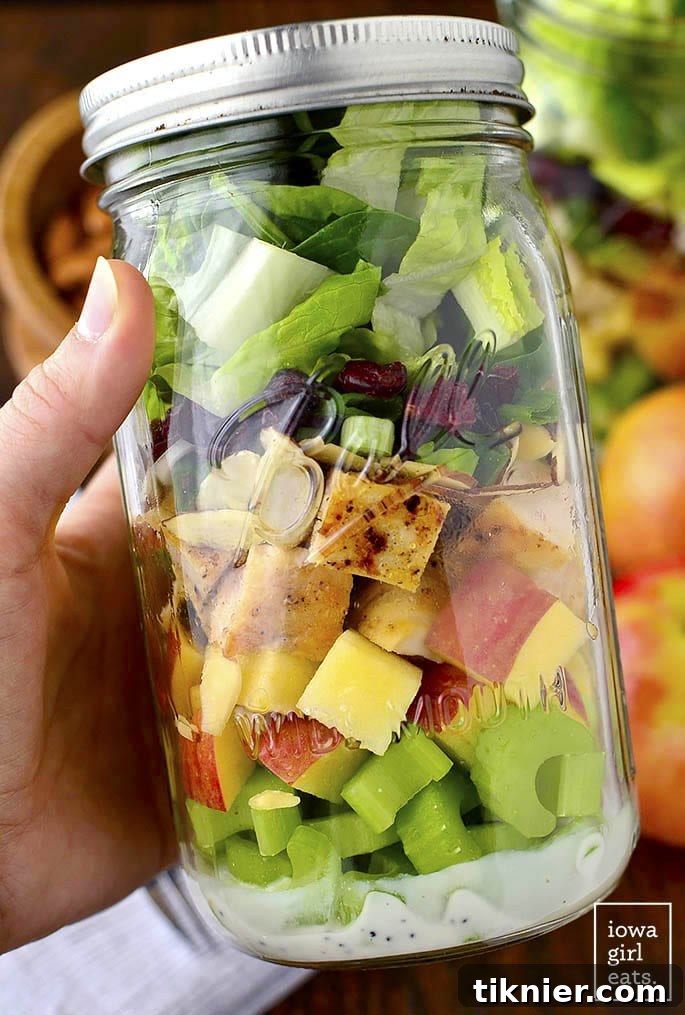 Beautifully layered Cranberry Almond Mason Jar Salads, displaying fresh ingredients like greens, apples, cranberries, and nuts.