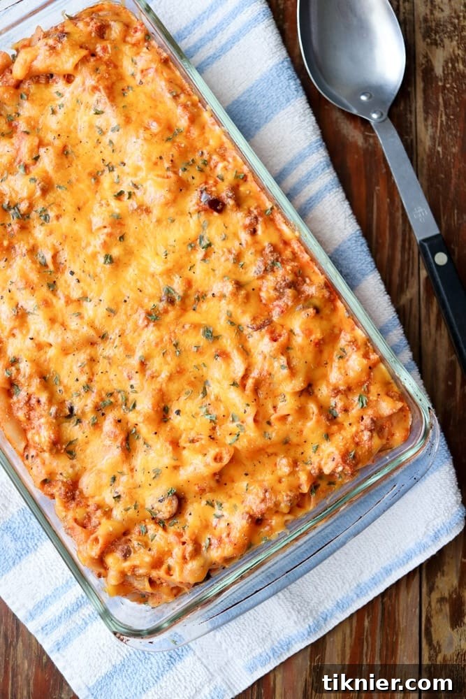 A close-up of a partially scooped gluten-free pasta casserole, showing layers of penne, ground beef, ricotta, and olives, with a golden cheese crust.