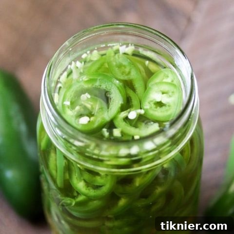 A close-up shot of perfectly sliced quick pickled jalapenos submerged in a clear brine within a mason jar, ready to be served.