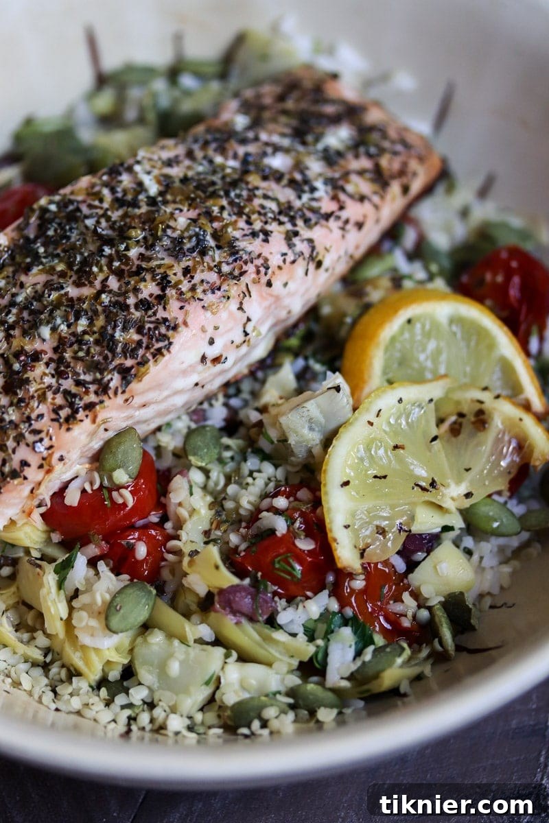 A close-up of a colorful Salmon Rice Bowl, featuring flaked salmon, roasted tomatoes, and green onions.