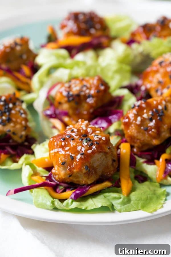 Light and flavorful Asian Chicken Meatball Lettuce Wraps topped with a colorful mango slaw, presented on a white plate.