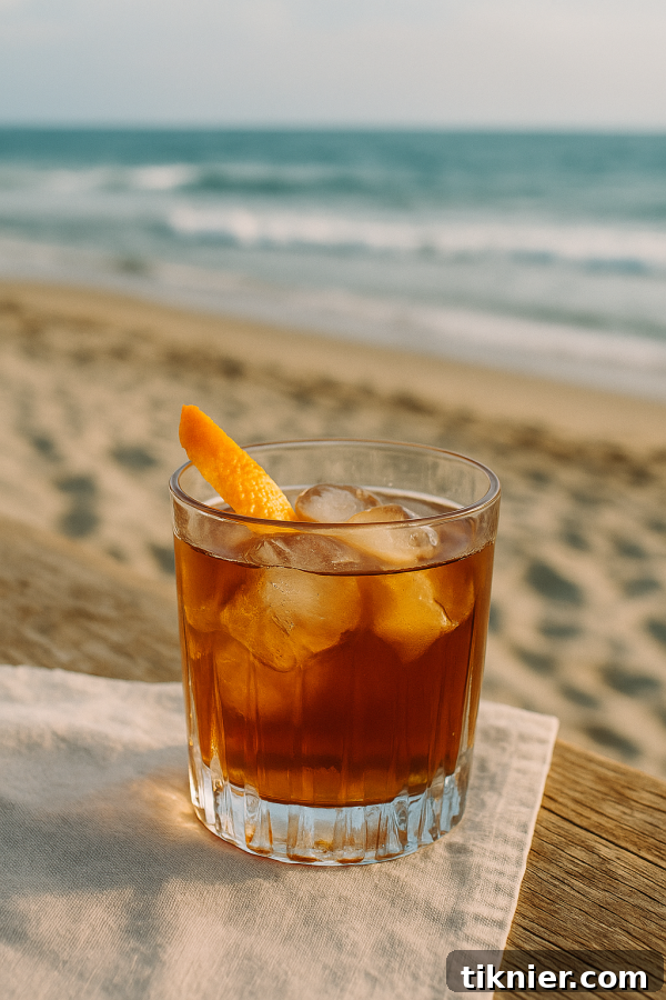 A classic Mezcal Old Fashioned cocktail garnished with an orange peel, served in a rocks glass with a large ice cube, against a warm, inviting background.