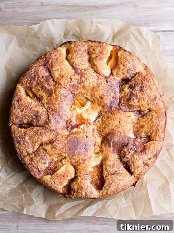 A slice of Best Ever Fresh Peach Buckle with a crumb topping, served on a white plate with a scoop of vanilla ice cream and a spoon.
