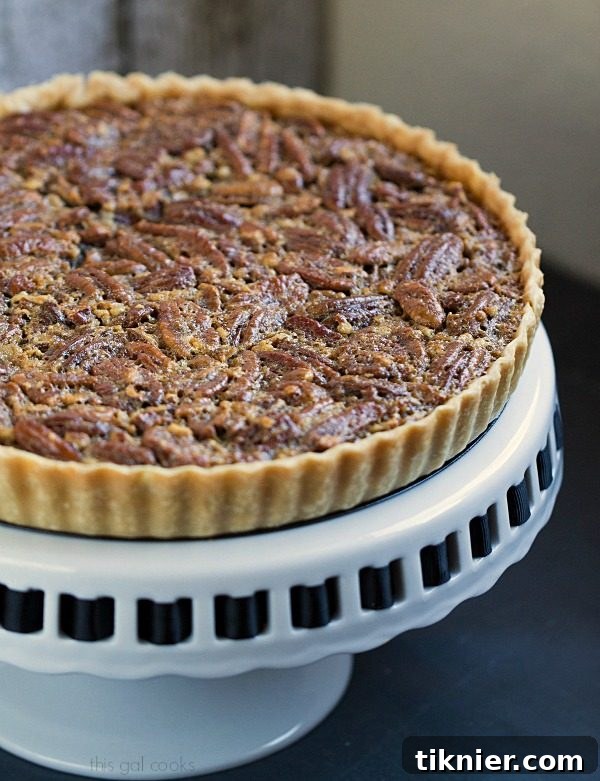 A slice of classic pecan pie tart, showing the rich, nutty filling and flaky crust, served on a white plate with a fork.