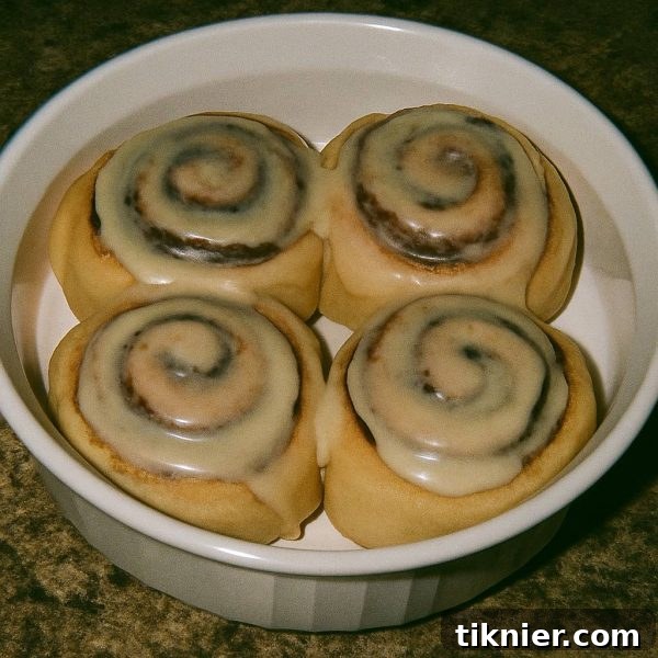 Warm, freshly baked Cinnabon-style cinnamon rolls with gooey cream cheese frosting, garnished with orange zest, on a rustic surface.