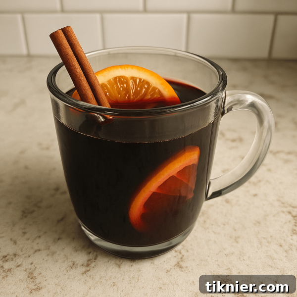 A steaming mug of vibrant ruby red mulled wine, garnished with a fresh orange slice and a cinnamon stick, sits on a rustic wooden surface next to whole spices.