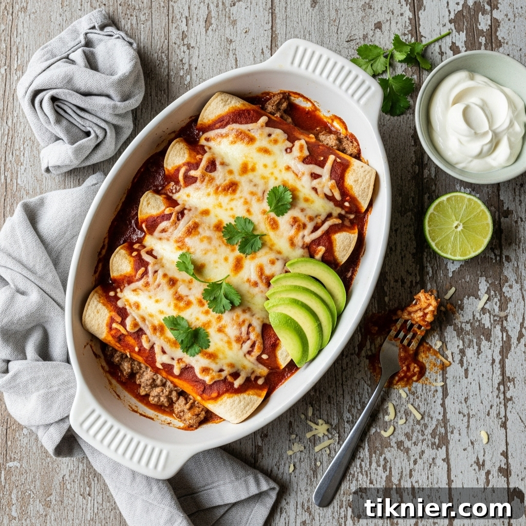 A close-up shot of a single creamy ground beef enchilada, topped with melted cheese and a dollop of sour cream, garnished with fresh cilantro, ready to be enjoyed.