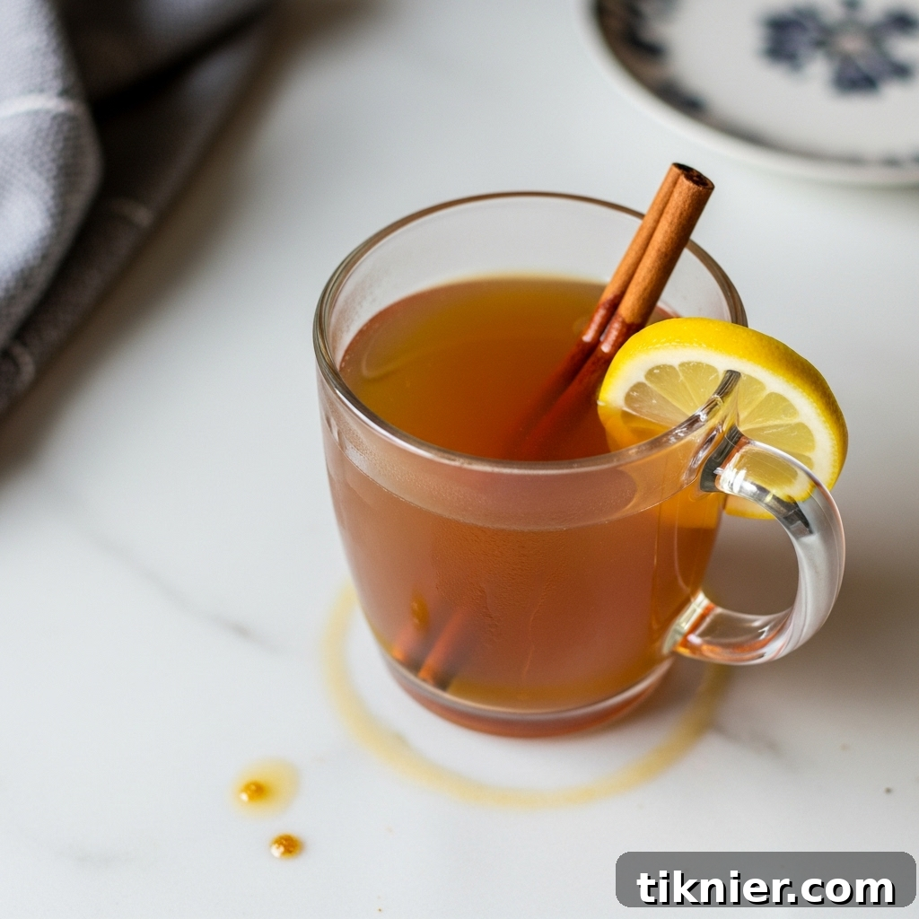 Sip on Genius: The Brown Butter Toddy 2 Steaming Brown Butter Hot Toddy in a clear mug, garnished with a cinnamon stick and lemon wheel.