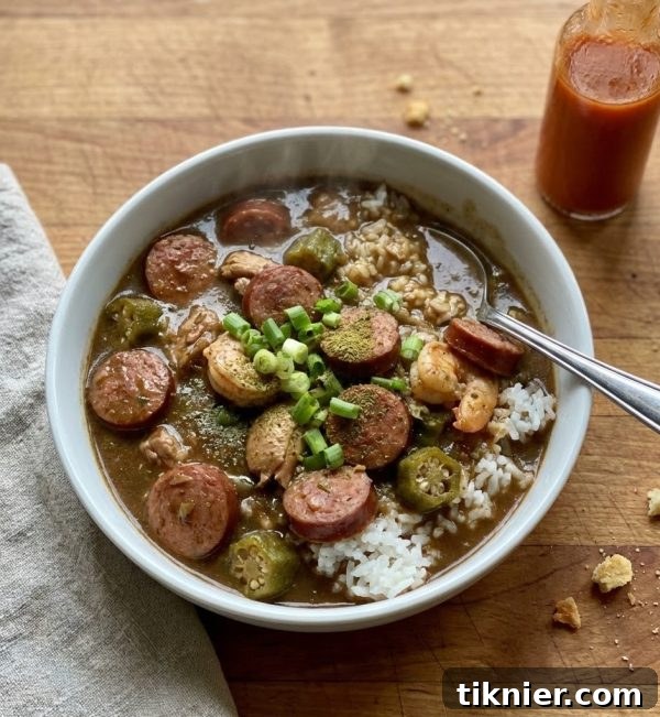 Close-up of a richly colored Gumbo soup in a bowl, with sausage, chicken, shrimp, and okra visible, garnished with green onions.