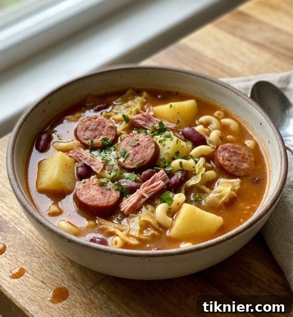 A close-up of Portuguese Bean Soup in a bowl, showcasing the rich texture and ingredients like ham hocks, sausage, beans, and fresh parsley garnish.